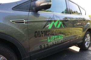 Side view of a gray SUV displaying a green mountain logo and 'Olympic Concrete Lifting' advertising.