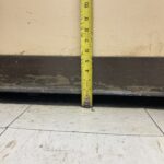 Measuring tape held vertically against a wall showing height from floor to about 10 inches, with a black baseboard below.