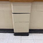 Close-up of a beige concrete support column made of stacked blocks against a beige wall and tiled floor.
