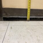 Yellow measuring tape extended vertically from the floor against a beige wall with a dark baseboard, showing about 8 inches.